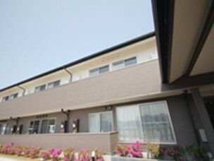 ピンクの花が建物の周りに植えられている。２階建ての建物は日当たり良好でベランダも付いている。