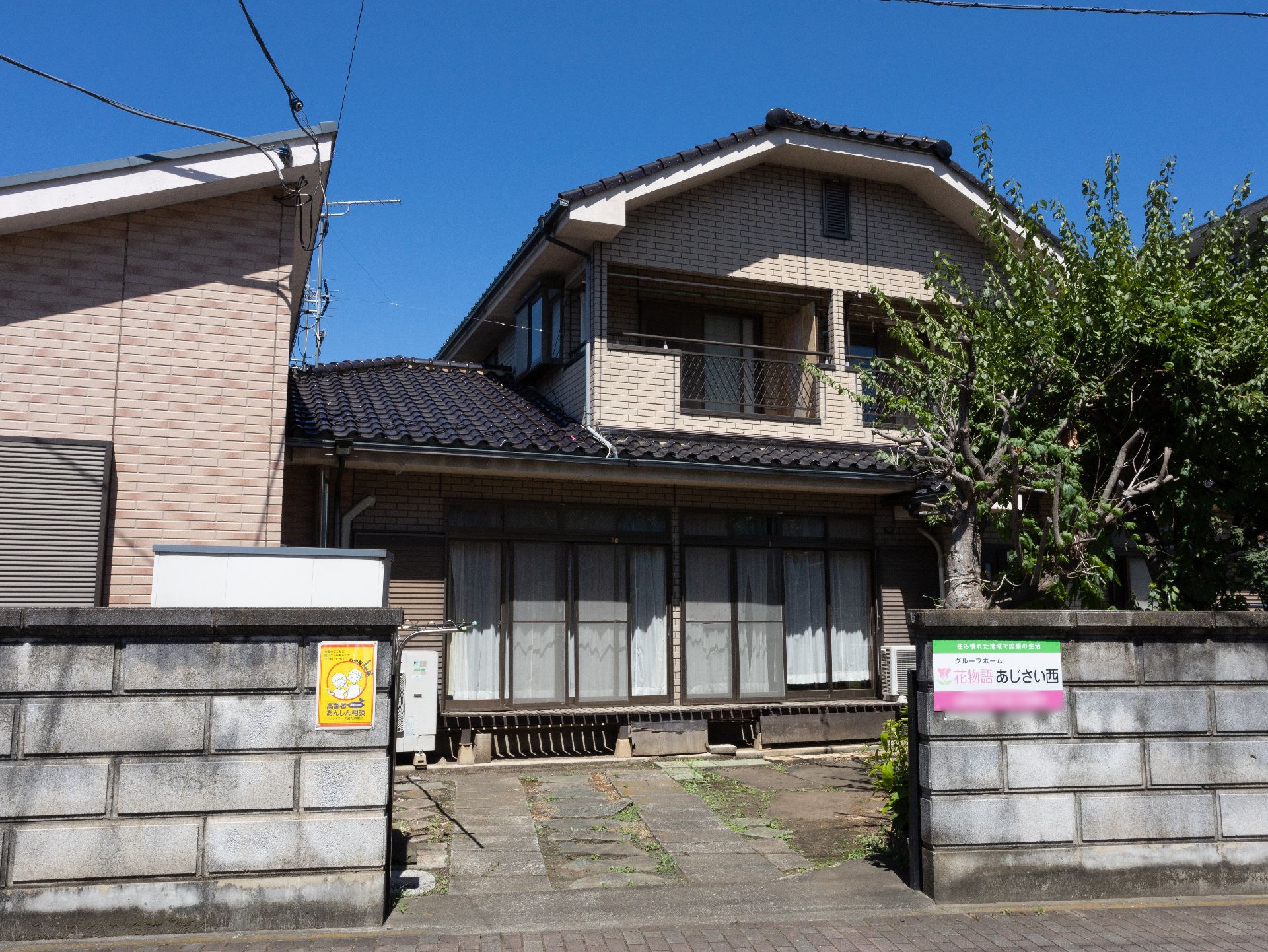 瓦屋根が付いた家庭的な雰囲気の住まい。ブロックへの周りには緑が多く、道に面している。