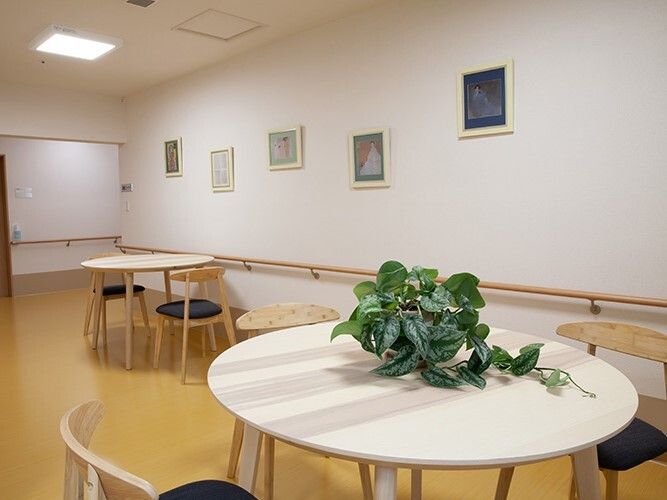 白い丸テーブルのセットが二組置かれた共有スペース。観葉植物や絵画などが飾られている。