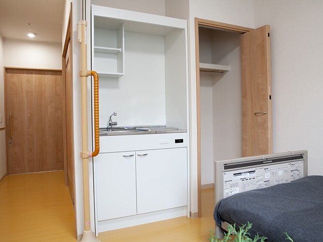 フローリングのシンプルな居室。キッチンやクローゼット、寝具付きのベッドなどが付いている。