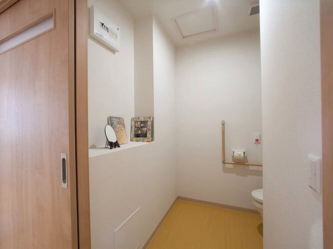エル字型の手すりが設置されたトイレ。オレンジの呼び出しボタンもつき、写真などが飾られた棚もついている。