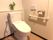 呼び出しボタンや手すりが付いたシンプルなトイレは白を基調としていて、便座の後ろの棚には環境植物が置かれている。