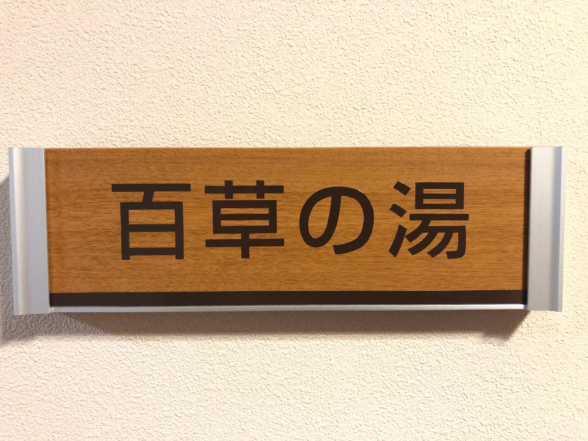「百草の湯」と書かれた木製のプレートに黒い文字が書かれたものが飾られている。