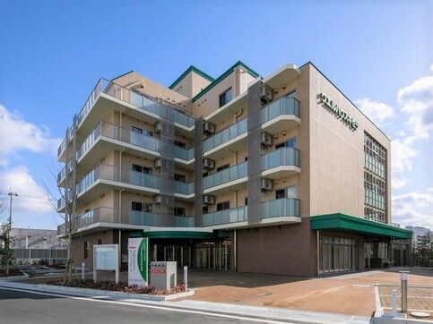 7階建ての建物はエル字型でベランダが各フロアにつき、玄関にはグリーンの屋根が設置され、敷地内には駐車スペースもある。