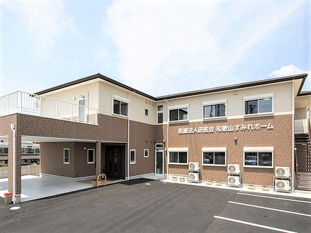 2階建てで広い駐車スペースが付き、フロアごとに外壁の色が異なる。周囲には住宅地もある。