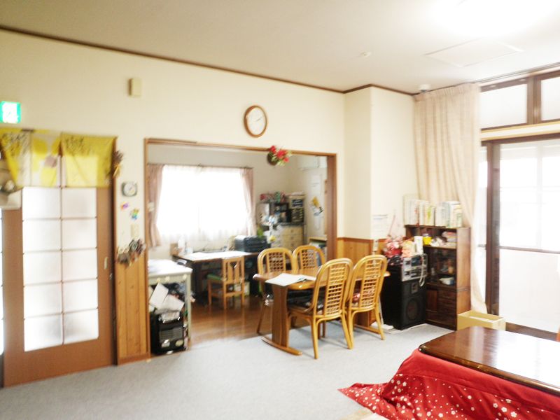 事務用品が置かれた部屋に隣接する場所にある、コタツやダイニングテーブルが置かれた部屋