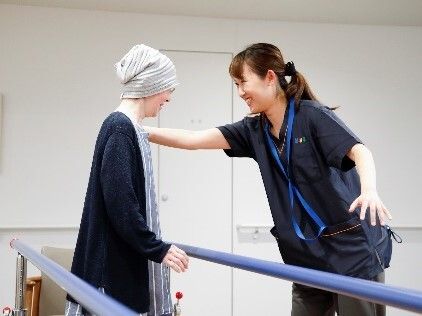 緑あふれる屋外で車いすに乗って散歩を楽しむ男性入居者とエプロン姿の女性スタッフ。