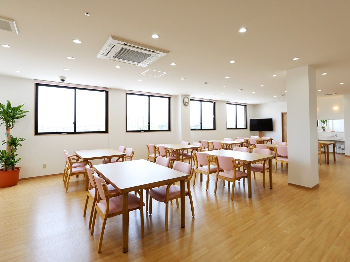木製のダイニングテーブルが複数置かれ、ぬくもりが感じられる明るい食堂。窓がたくさんついている。