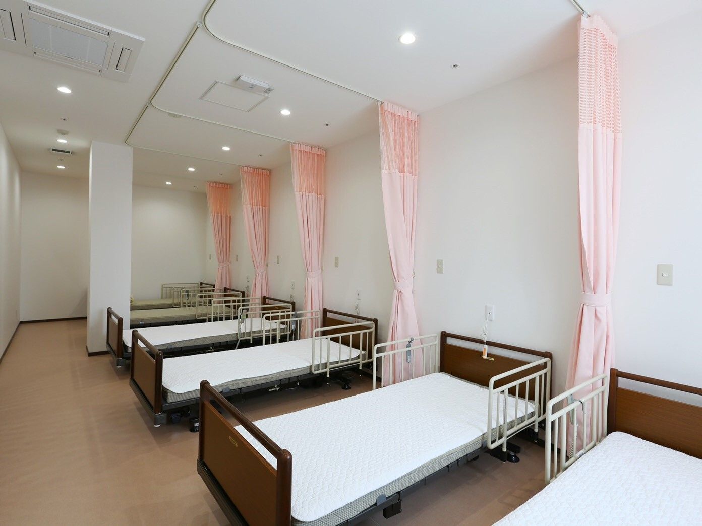 多くの介護用ベッドが並び、ベッド間をカーテンで仕切った部屋