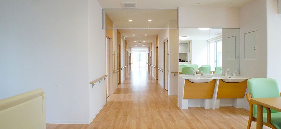 まっすぐな廊下には両側に手すりが付き、居室ドアが並び、手前にはダイニングテーブルが置かれた共有スペースがある。