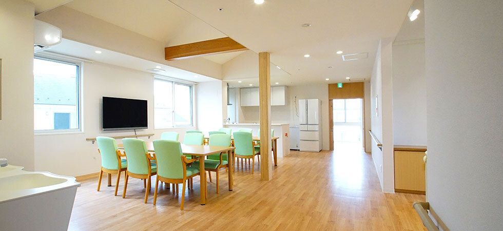 木製のダイニングテーブルが二組置かれたフローリングのダイニング。対面式のキッチンも付いている。