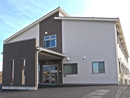 2階建ての建物には三角屋根が付き、グレー系でまとめられ落ち着いた雰囲気。周りには建物はなく、日当たりもよい。玄関には車寄せも付いている。