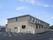 ベージュ系の外壁の２階建ての建物は日当たりのいい場所に建っていて、手前には洗濯物干し場がある。