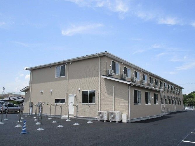 洗濯物干し場がある敷地内には広い駐車場もあり、ベージュの外壁の2階建ての建物がある。