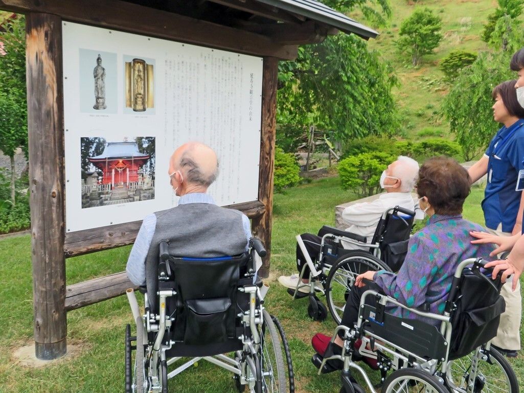 車いすの高齢の男女が熱心に観光地の説明文を呼んでいる様子。近くには女性スタッフが付き添っている。