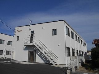 白を基調とした2階建ての建物を側面から見た様子。側面には屋外階段が設置され、周りにはたくさんの木もある。