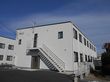 白を基調とした2階建ての建物を側面から見た様子。側面には屋外階段が設置され、周りにはたくさんの木もある。