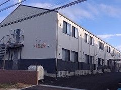 広い駐車場が付いた2階建ての建物は白とダークグレーで、外壁にはホーム名が書かれている。