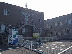 ダークグレーの2階建ての建物は玄関に自動販売機が設置され、広い駐車場もある。