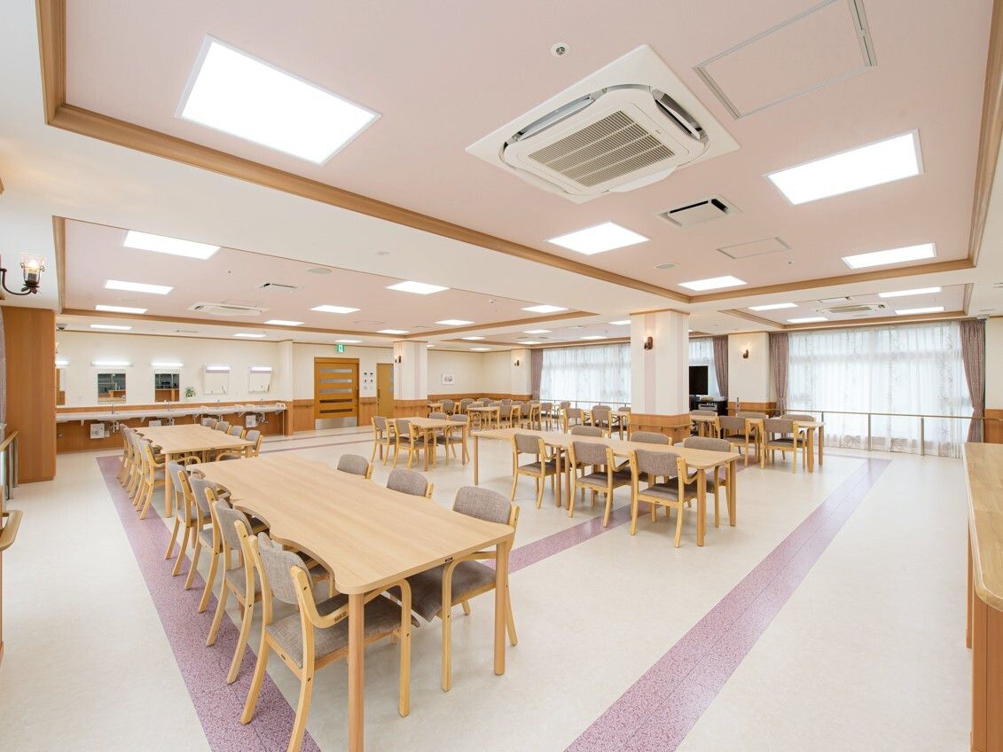 ブラウンの椅子がセットされた木製のダイニングテーブルセットが複数置かれた食堂。大きな窓がある。