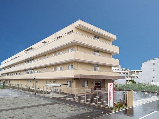 4階建ての建物はベージュ系の外壁で敷地内には駐車場があり、屋根付きの駐輪場も設置されている。