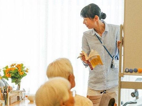 笑顔で高齢者に話しかけているシャツを着た女性がホワイトボードの横に立っている。