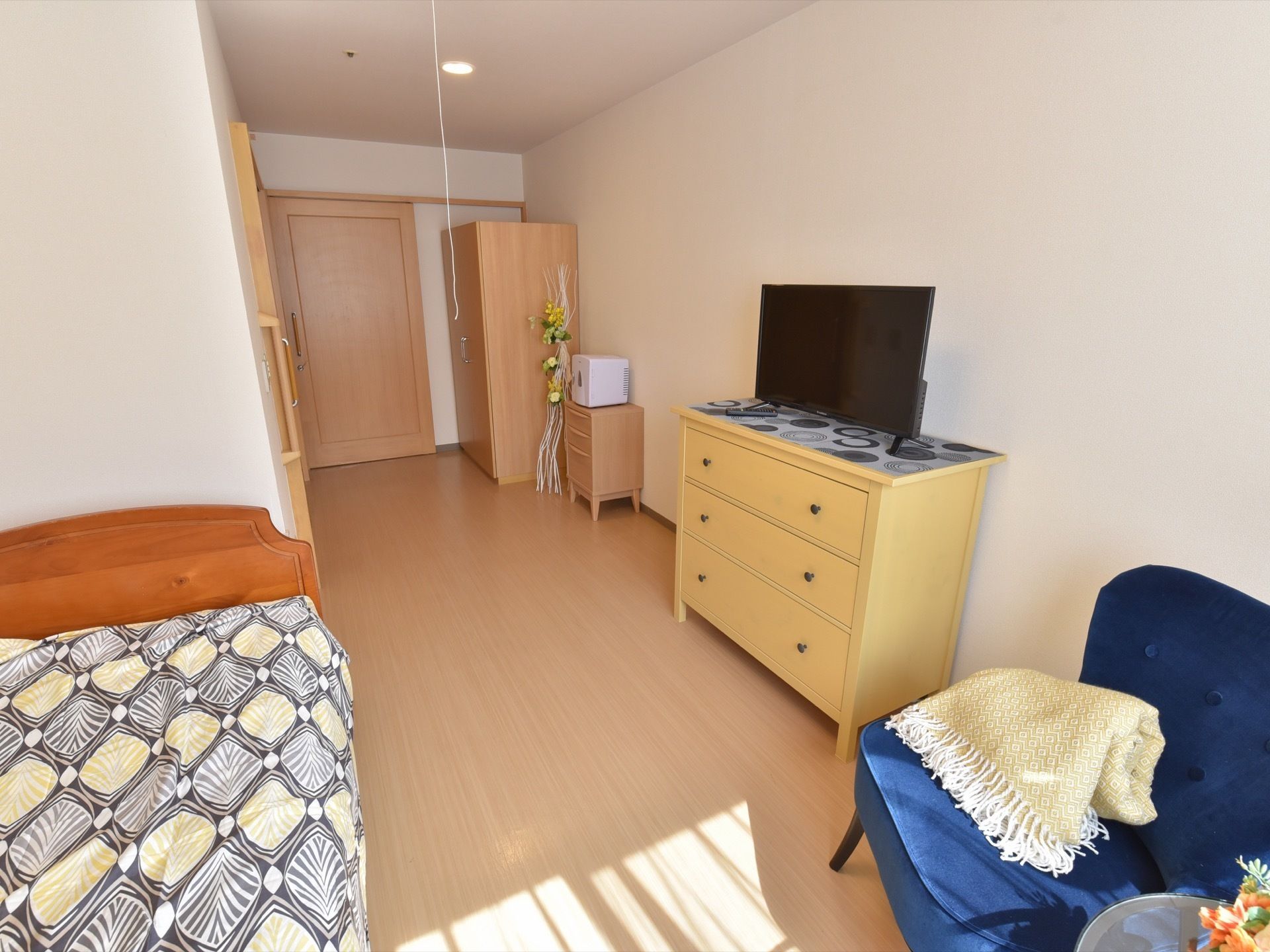 居室には、窓があり明るい。居室扉からはベッドが見えにくく設置され、入居者様の好みの家具など配置されている。
