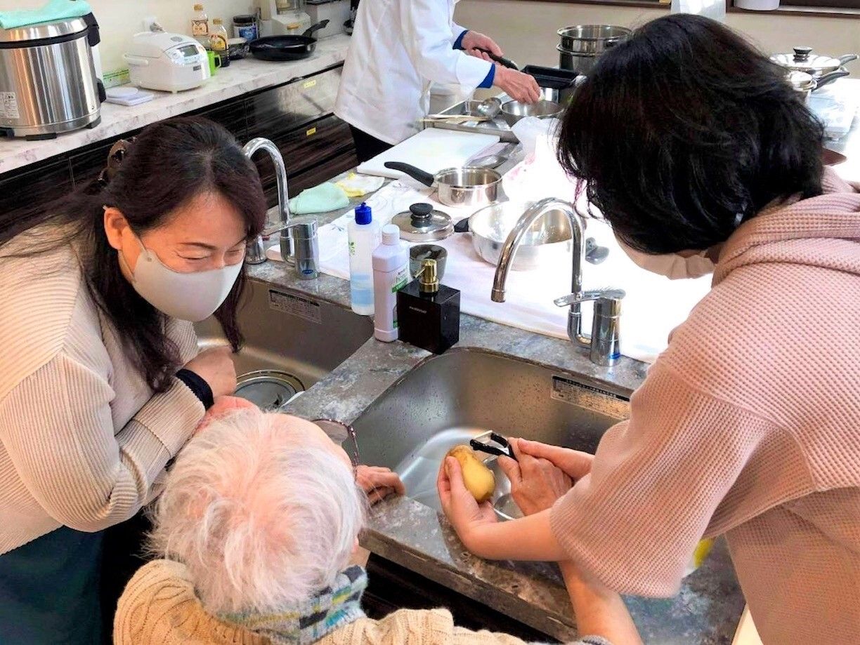 スタッフにサポートされながら炊事をする高齢女性