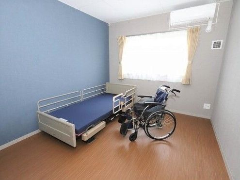 ブルーの壁が印象的な個室の部屋には車いすやベッドがあり、窓にはカーテンがついている。