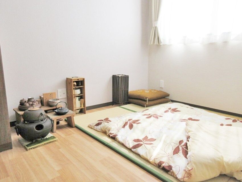 フローリングの部屋には畳が敷かれ、布団が敷かれている。座布団や茶道の道具のようなものが置かれている。