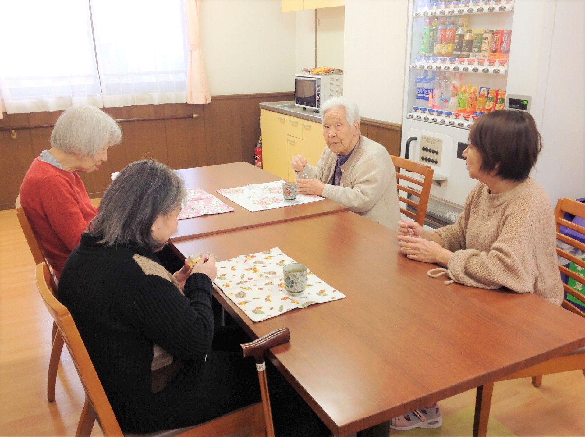 四人掛けのテーブルと椅子に座ってだんらんしている様子。施設内の高齢者の様子
