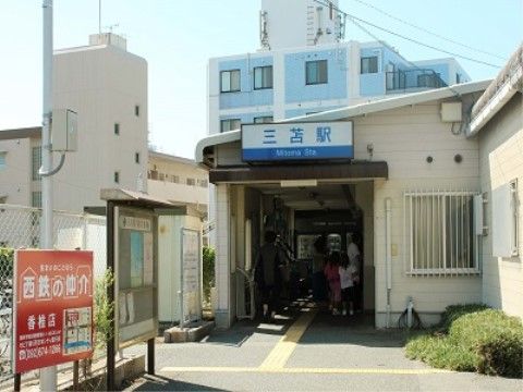 白い外観の駅舎がある。青い文字で駅名が書かれた看板が、設置されている。地面には黄色い点字ブロックが敷かれている。