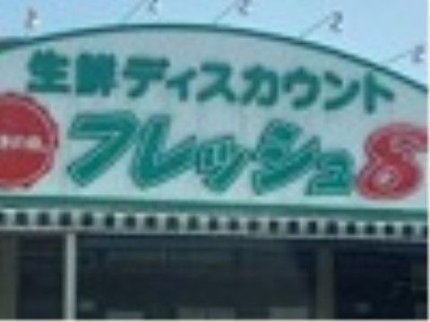 生鮮食品を取り扱っているスーパーがある。白い背景に緑色と赤い文字でお店の名前が書かれた看板が設置されている。