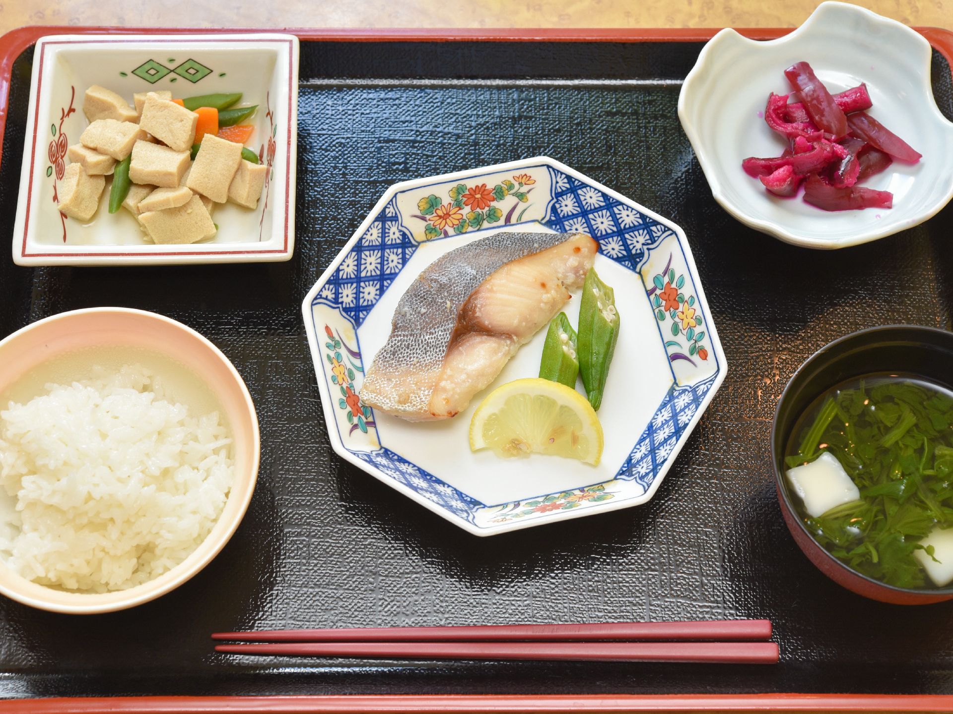 トレイにセットされた食事。メインは焼き魚のオクラ添え、小鉢とお椀とお新香が付いている。陶器の皿を用いている。