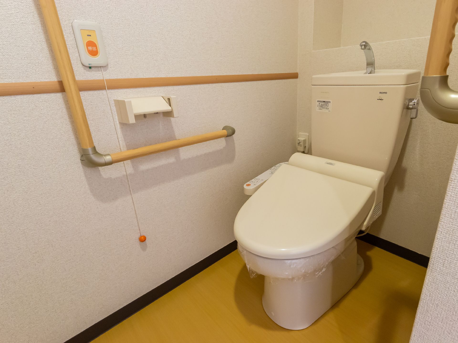 眼鏡をかけた高齢男性が福祉車両から下りようとしているところを若いスタッフが手を貸し、手伝っている。