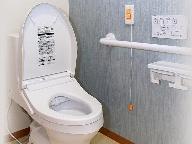呼び出しボタンがついたトイレには手すりがあり、温水便座が設置されている。壁の一面がブルーで落ち着いた雰囲気。