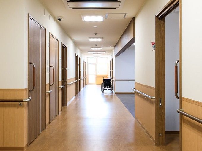 居室のドアが並ぶまっすぐな廊下。突き当りには窓があり、廊下は全域手すりが設置され、車いすが右端にある。