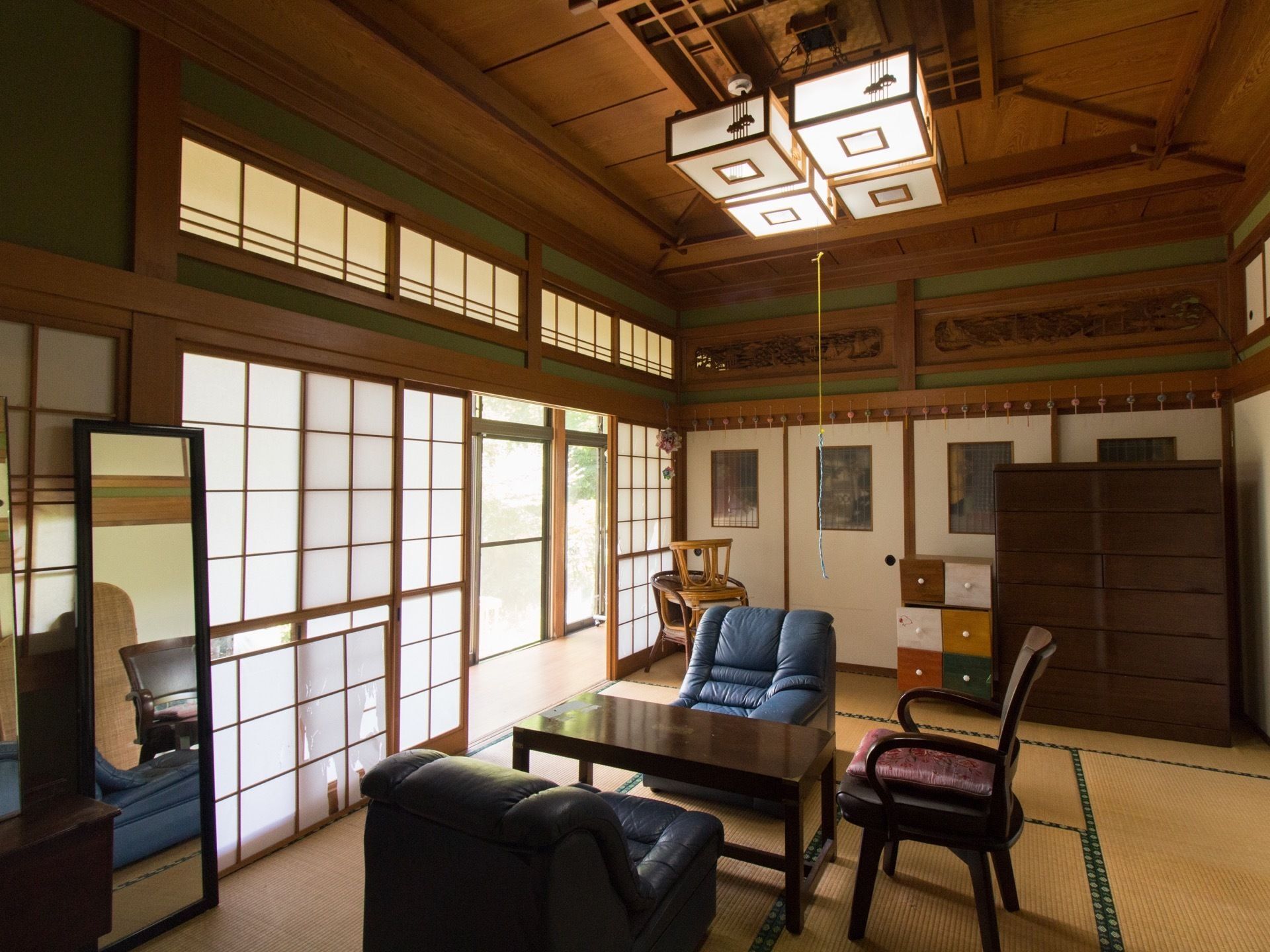 障子が設置された畳敷きの部屋にはブルーの一人用のソファの応接セットが置かれ、重厚感のある収納家具もある。