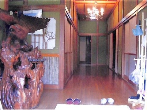 木彫りの大きな置物が置かれた玄関にはマットが敷かれ、スリッパが置かれている。まっすぐな廊下が続き、花弁は砂壁のような緑色。