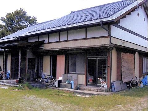 グレーの瓦が付いた和の建物。玄関には屋根があり、勝手口のそばには犬が座っている。