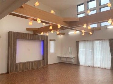 大きなスクリーンが設置された共有スペース。家具は置かれていないものの梁にはたくさんの照明が付き、窓にはカーテンが付いている。