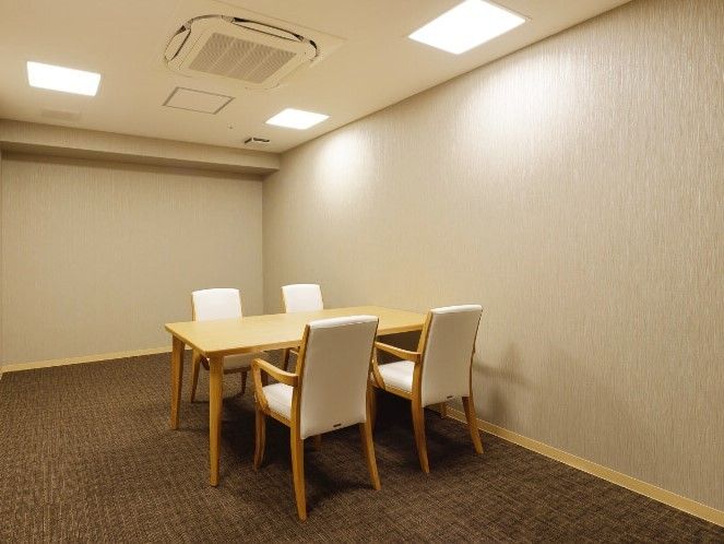 シンプルなブラウンのカーペット敷きの部屋には装飾品はなく、白い椅子が4脚セットされたテーブルがある。
