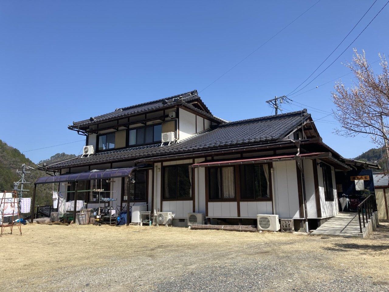 緑に囲まれたホームの敷地内には庭があり、グリーンのパラソル付きのテーブルセットが置かれ、帽子をかぶった入居者がテーブルを囲んでいる。