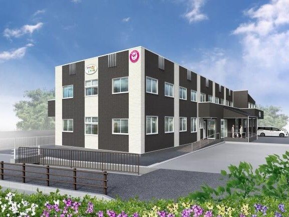 白とダークグレーの３階建ての建物は日当たりのいい場所に建っている。玄関先には車寄せがあり、人の姿もある。