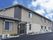 レンガ調のブラウンの外壁。手前の建物は平屋建て、奥には２階建てがあり、建物の前には車が一台止まっている。