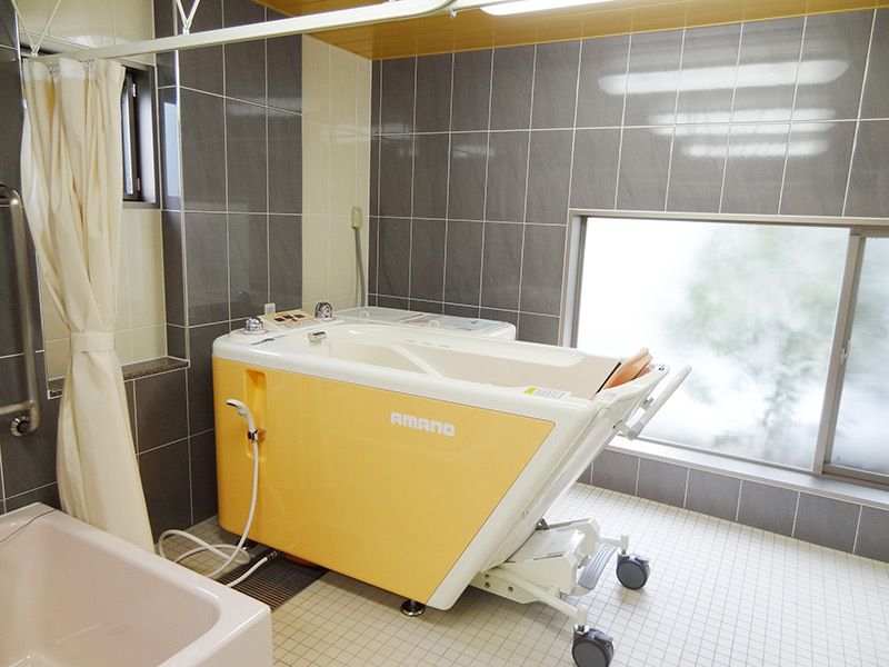 白と黄色の機械浴が置かれたタイル張りの浴室。重度の人も入浴できる設備がある。