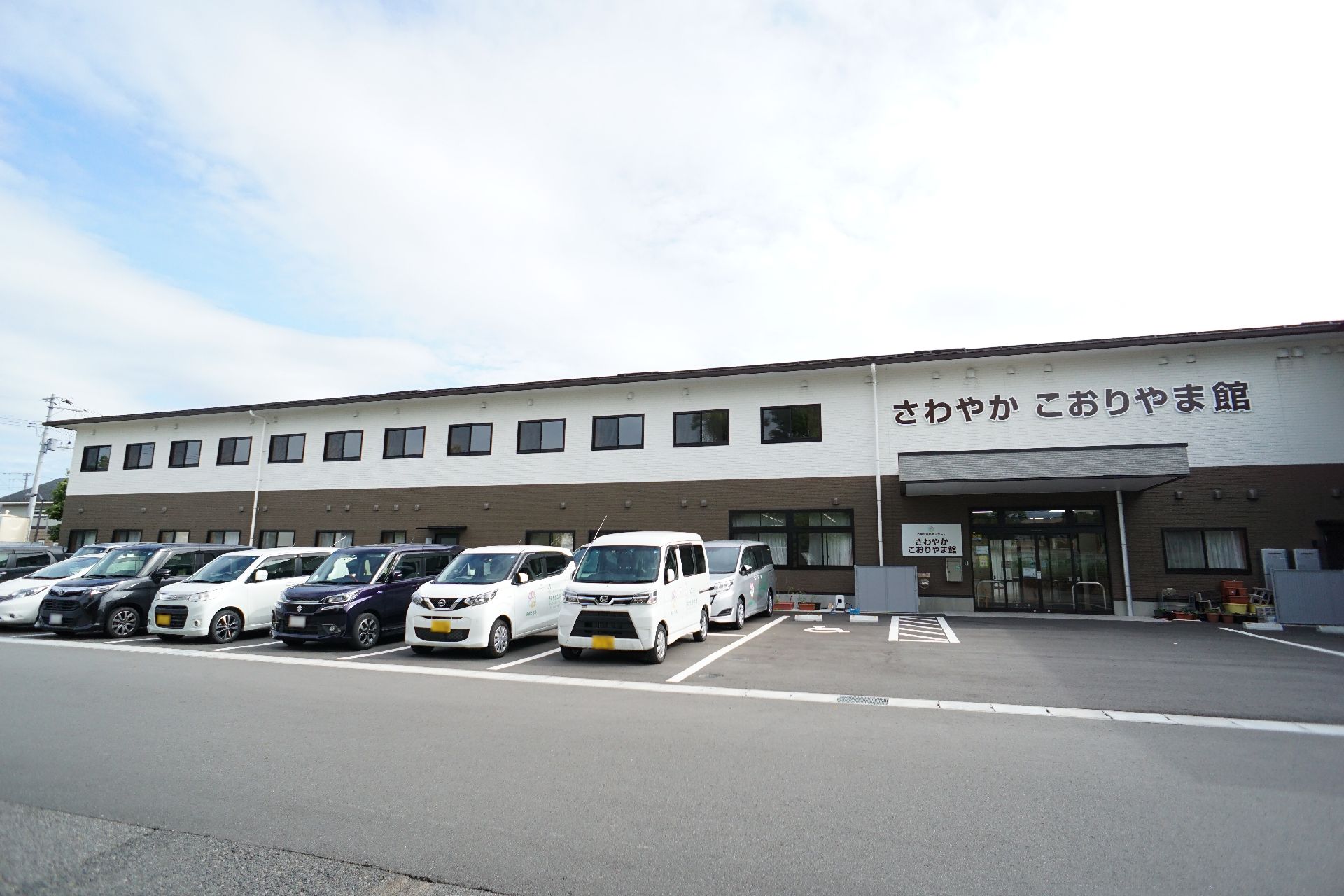 車がたくさん止まった駐車場に隣接している白とブラウンの外観で２階建ての建物