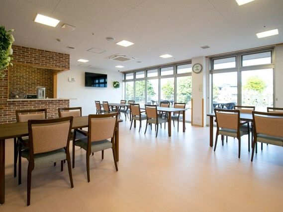 ベージュの椅子がセットされたダイニングテーブルセットが複数置かれた食堂にはテレビも設置されている。