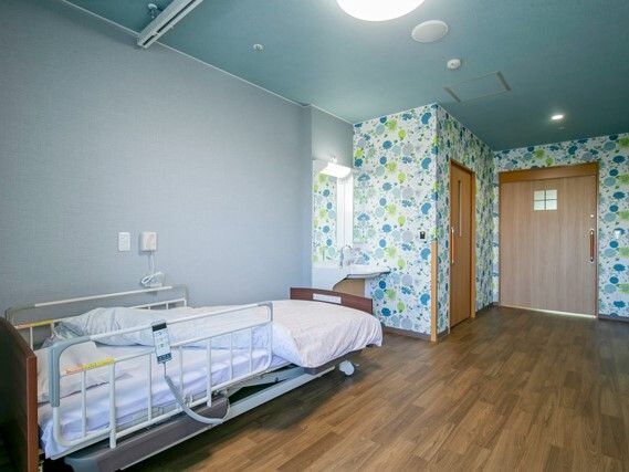 グリーン系のクロスが貼られた明るい雰囲気のフローリングの部屋には寝具付きのベッドが置かれ、緊急通報装置もある。