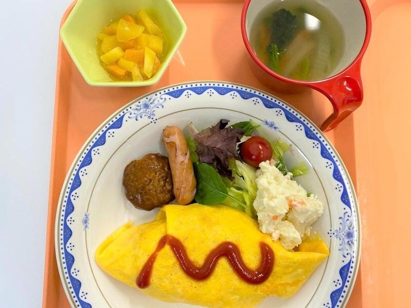 カットフルーツやスープが添えられ、メインのオムライスの周りにはハンバーグやソーセージ、ポテトサラダなどがある。